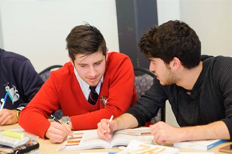 Two high school students look at a textbook together